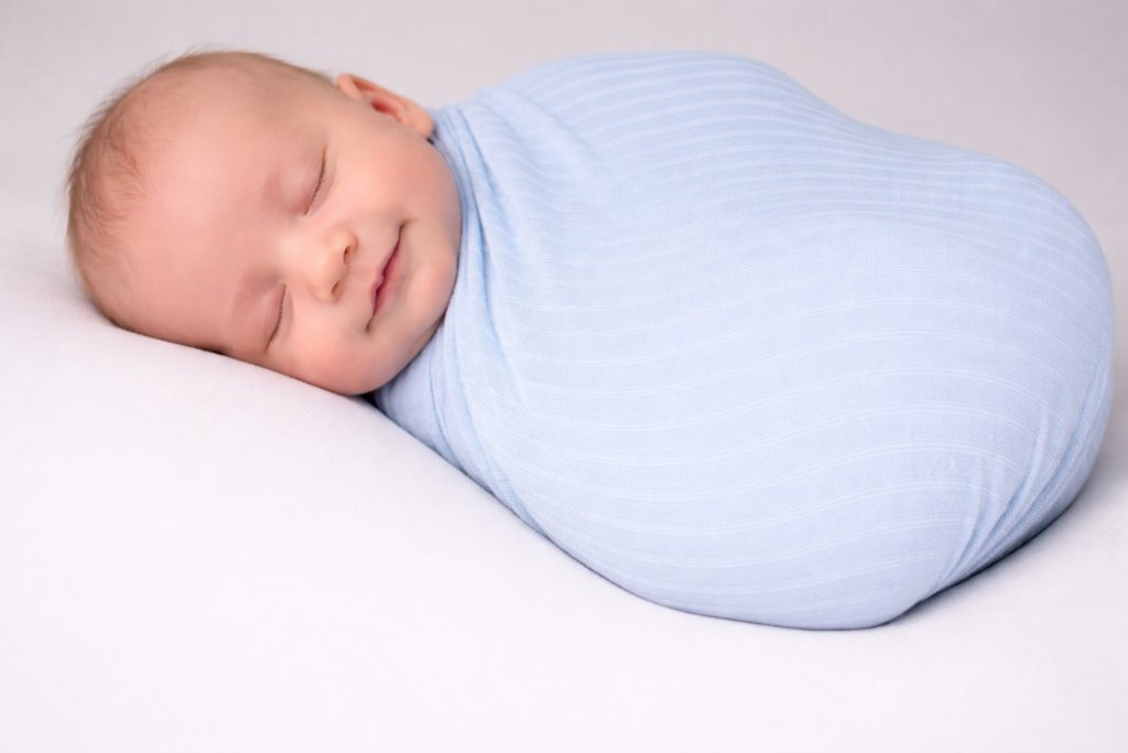 Swaddle newborn to sleep concept with a peacefully sleeping Caucasian baby wrapped in a soft sky blue swaddle on a white background